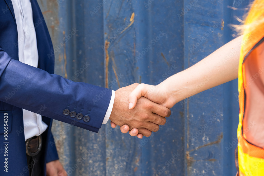 Businessman and engineer woman shake hands as hello in the container yard shipping area. Shaking hands after the inspection or investigation are complete. Industrial and business concept
