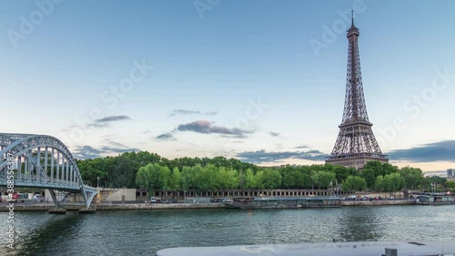 Eiffel tower with Debilly Footbridge and Jena bridge over Seine river evening timelapse from waterfront, Paris, France. Ship on the river and reflections in water photo