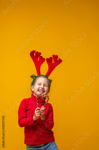 Happy little girl 4 years old in reindeer antlers on a bright yellow background.