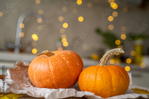 Two pumpkins lie on crumpled paper on a white wooden table against a garland