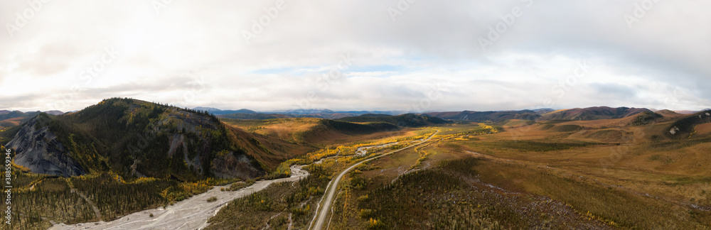 Panoramic View of Scenic Winding Road surrounded by River, Mountains and Valley in Autumn on a Cloudy Day. Aerial Drone Shot. Taken near Dempster Highway, Yukon, Canada.