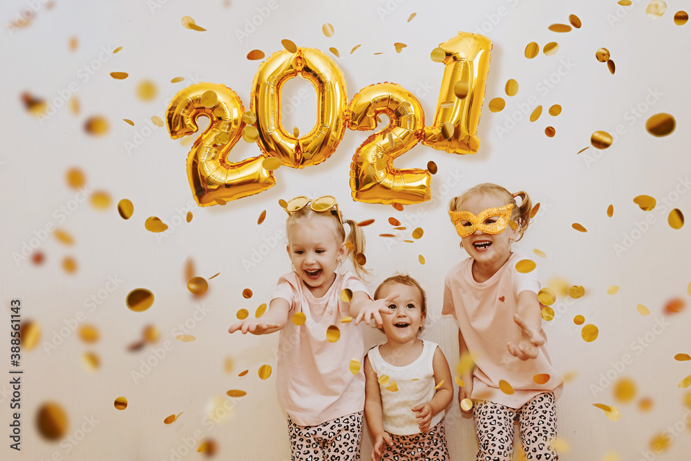 Three little girls are enjoying the flying golden confetti. Celebrating at home 2021. Concept for Christmas and New Year. - obrazy, fototapety, plakaty 