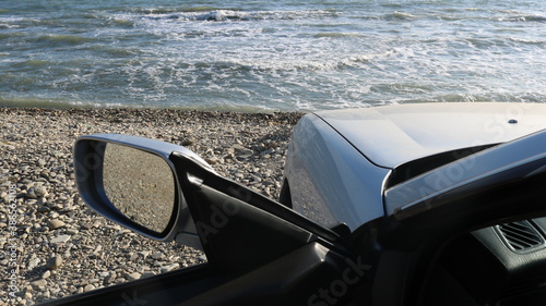 the open door of a silver car standing on the seashore as a symbol of freedom of travel and the happiness of free choice of lifestyle, enjoyment of auto tourism on the ocean coast