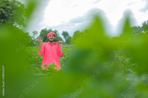 Young indian farmer holding farm equipment in hand at cotton field photo