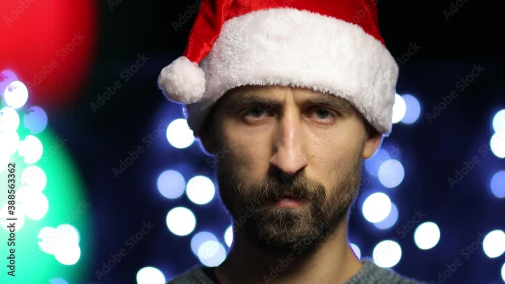 Young bearded European man in Santa hat, showing STOP gesture with his hands. angry european man wearing a Santa hat shows a STOP gesture on a bokeh background. video close-up. Young bearded European man in Santa hat, showing STOP gesture with his hands. angry european man wearing a Santa hat shows a STOP gesture on a bokeh background. video close-up.