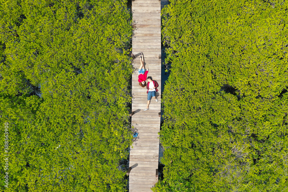 Aerial view of a romantic couple, a man and woman in red, lying on the ground in the green meadow in Large mangrove.. Love and dating concept