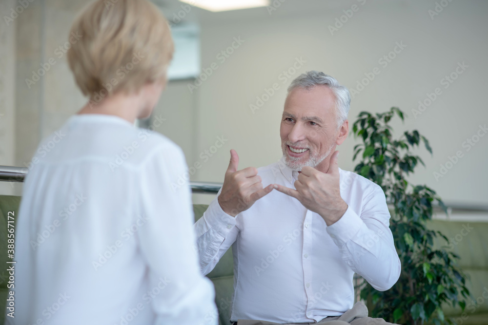 Bearded gray-haired man talking with blonde woman using sign language Bearded gray-haired man talking with blonde woman using sign language