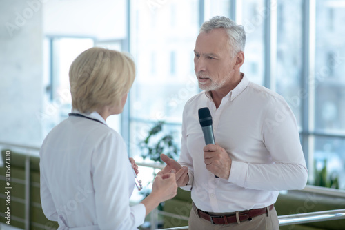 Gray-haired male journalist interviewing blonde female doctor