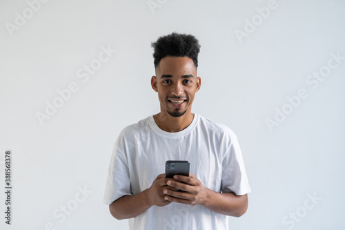 Happy African American man using phone, looking at screen, chatting with friends in social networks or reading pleasant news in email, standing isolated on white background