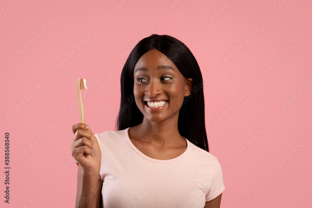 Portrait of lovely black lady with shiny smile holding eco toothbrush with paste over pink studio background Portrait of lovely black lady with shiny smile holding eco toothbrush with paste over pink studio background