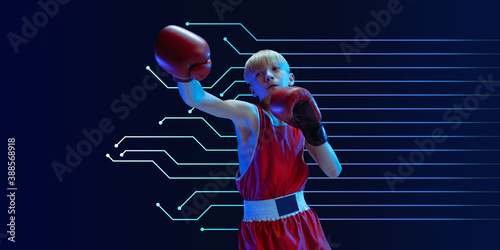 Teenager in sportswear boxing isolated on blue studio background in neon light. Novice male caucasian boxer training hard and working out, kicking. Neoned modern artwork, cover, flyer designed.