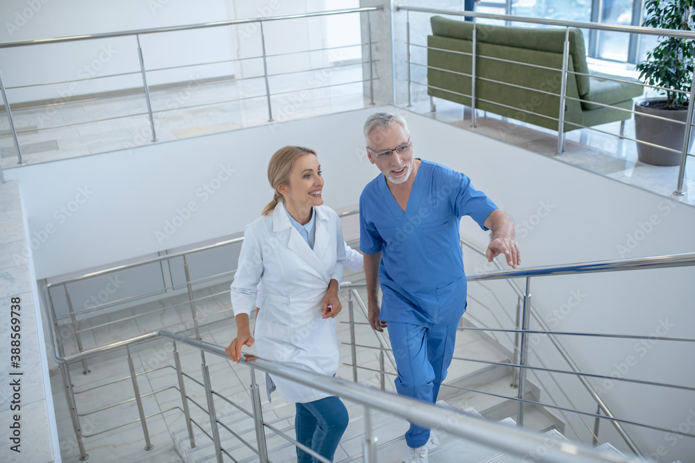 Male and female doctors walking upstairs, having friendly conversation Male and female doctors walking upstairs, having friendly conversation