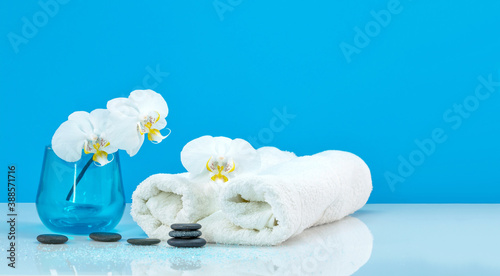 Spa Moth orchid with soft towel and massage stones setting. Zen pebbles balance. Spa and healthcare concept on blue Background