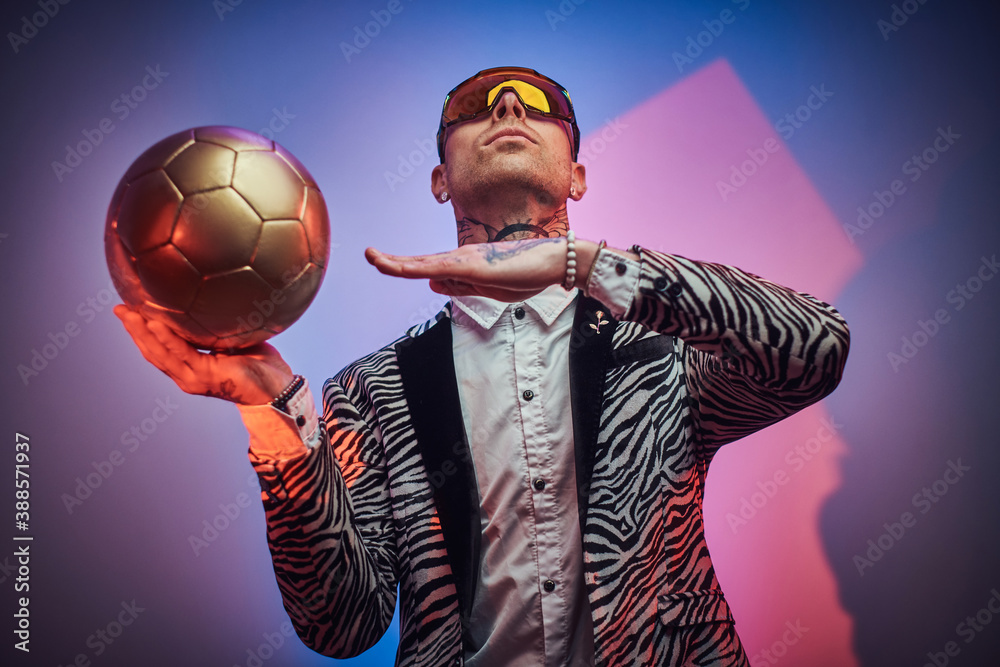 Plakat Futuristic man in suit with short haircut and eyewears poses with golden ball in colored abstract background.