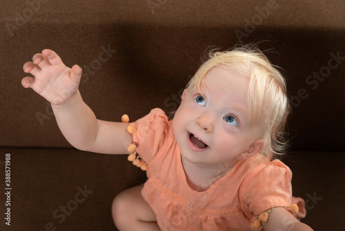 Portrait of little blonde girl who raised her hand and asks for something from an adult