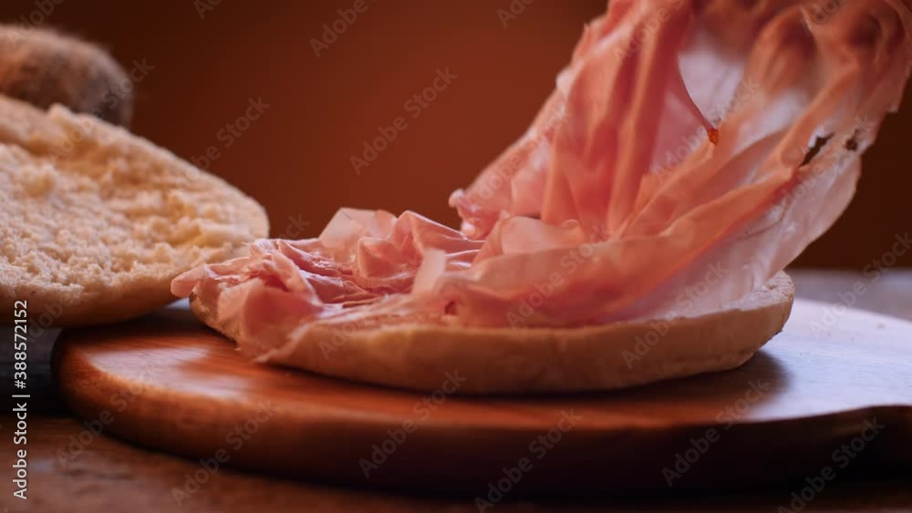 Italian mortadella sandwich on wooden cutting board. Rustic scene describing the filling of bread with sliced mortadella. Dolly and slow motion movement.