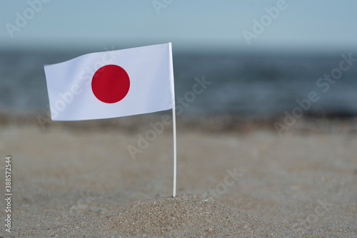 Flag of Japan on sea shore. White flag with red circle.