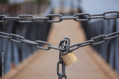 Strong chain with padlock blocks the way to a wooden bridge. Close up image with selective focus and shallow depth of field.