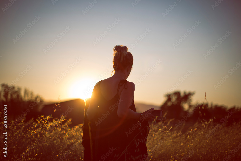 Woman from behind at sunset in field.