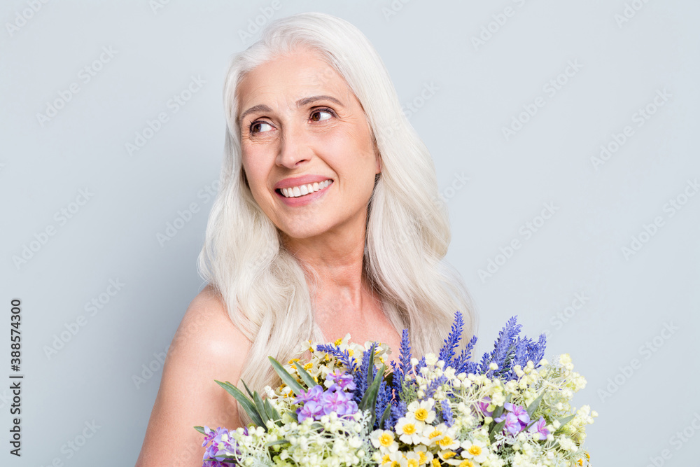 Photo of cute retired woman beaming smile hold big bunch wild flowers look empty space shy isolated grey color background Photo of cute retired woman beaming smile hold big bunch wild flowers look empty space shy isolated grey color background