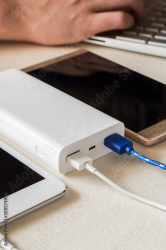 Power bank charges cell phone and tablet on desk. Universal external batter