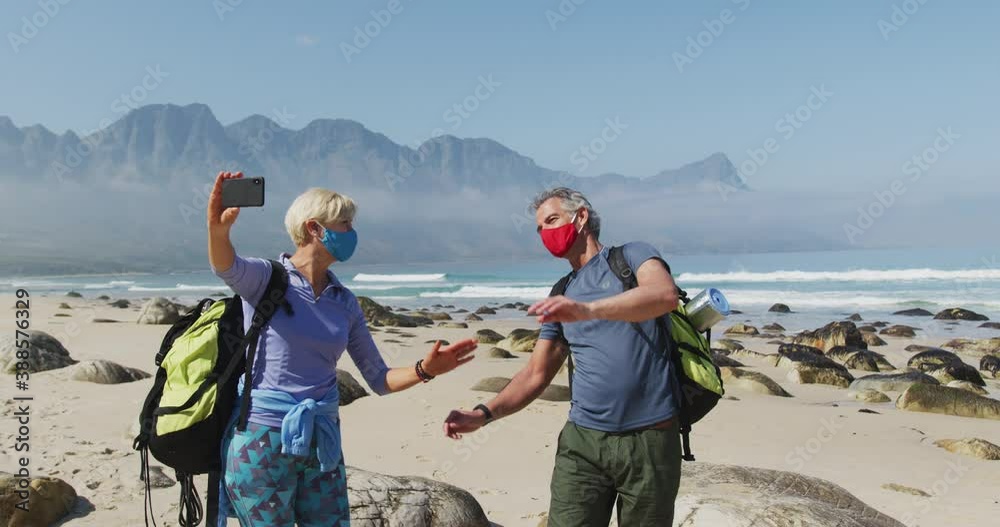 Senior hiker couple wearing face masks with backpacks waving while having a videocall on smartphone Senior hiker couple wearing face masks with backpacks waving while having a videocall on smartphone