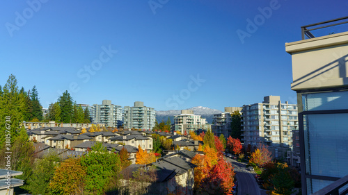 Crimson and orange clusters of fall colors throughout BC residential mountain community with backdrop of mountains with light snowfall
