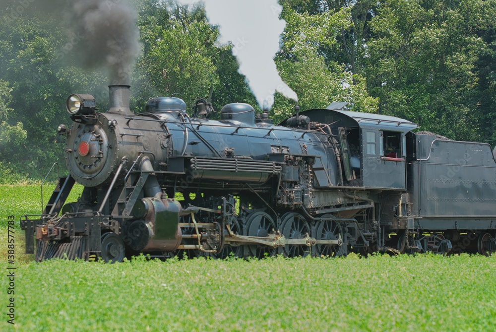 Naklejka premium Close Up of an Antique Steam Passenger Train Puffing along Amish Countryside with Green Fields