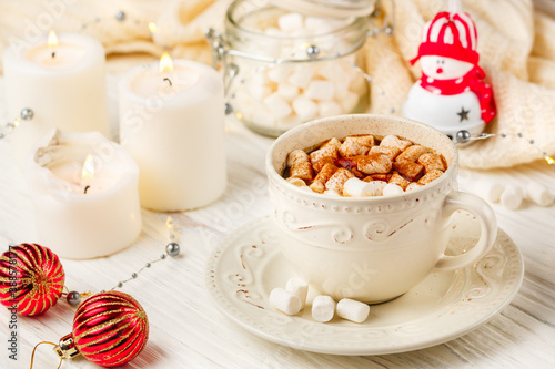 Coffee, cocoa, hot chocolate with marshmallows and cinnamon in a white Cup on a wooden table. New year. The concept of comfort and relaxation with candles, spices and Christmas toys. Selective focus