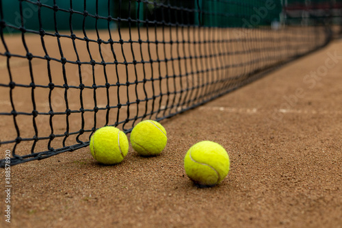 Three tennis balls lie side by side on a red clay court along the playing net. © Сергей Тарантино