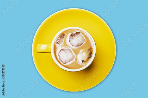 Ice coffee top view. Frozen latte with ice cubes. Yellow ceramic cup on yellow ceramic plate. Sweet sugar beverage milk drink.