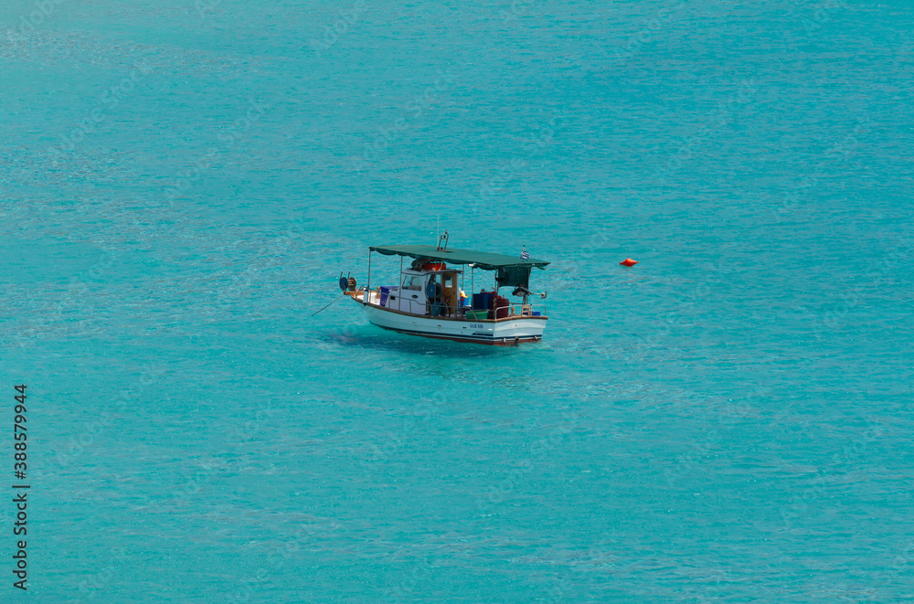 Simos bay at Elafonissos, south Greece. 
A peacefull scenery with turquoise water. A fishing boat stands alone on the water. A photo taken from a hill with zoom, isolating the boat.