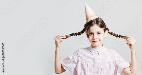 Funny dark-haired girl in a birthday cap in a trendy style. Smiling and fooling around. On a white studio background. Place for an inscription.