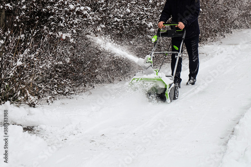 Human cleans snow off path with wireless electric snow blower after the winter snowfall photo