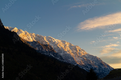 View at mountain Giona Greece. It is winter. The mountain at the backgrownd is snowy. At the foregrownd the mountain as a silhouette. At the right the blue sky with few clouds. Golden hour 