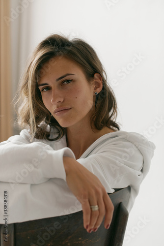Portrait of beautiful young woman with brown hair and clean bronze skin without makeup on white background. Natural and healthy look. Neutral interior. Soft light. 