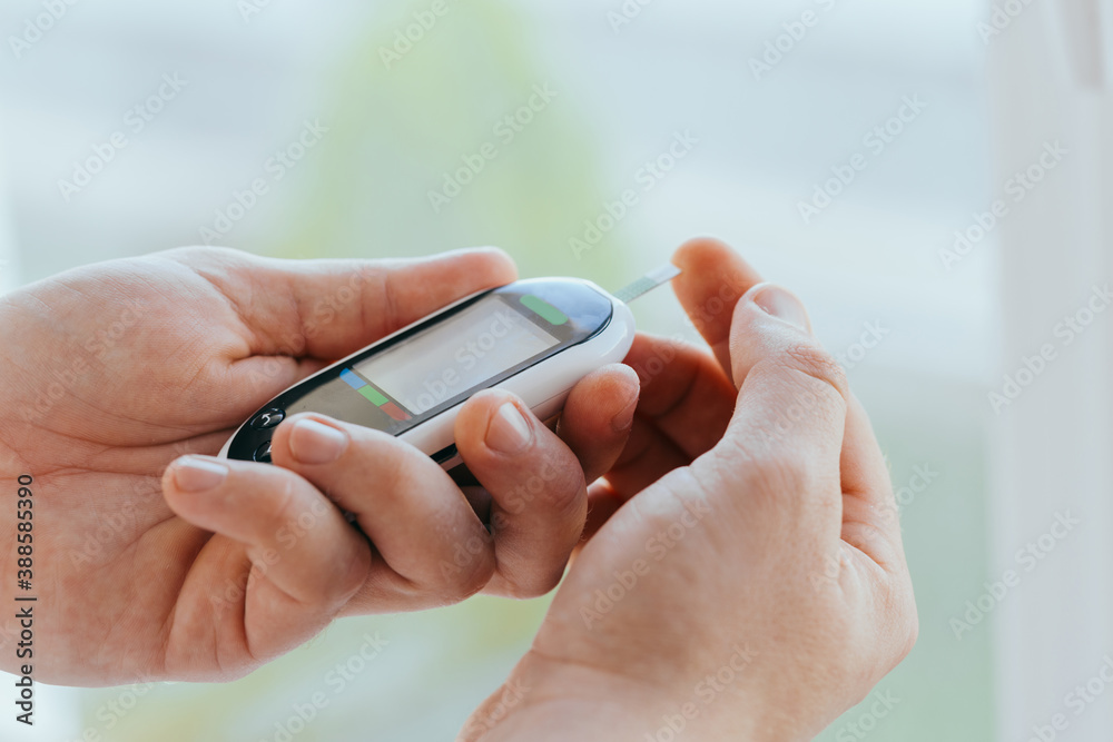 Fototapeta premium diabetes, healthcare - close up of a man with a glucometer and a test strip checking blood sugar at home