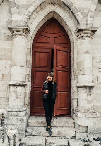 young woman in a leather jacket near the entrance to the ancient wooden door of a gothic temple © Виктория Бычкова