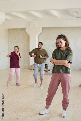 Portrait of young instructor looking at camera while standing in dance studio together with her team