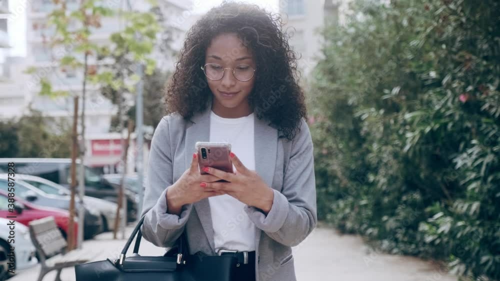 Video of pretty young business woman using her smart phone while drinking coffee walking down the street.