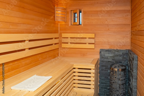 Compact sauna interior. Empty sauna wellness. Stones in a metal mesh inside the sauna. Steam room for wellness treatments. Classic steam room interior. Wooden walls and bench  stoun heaters.