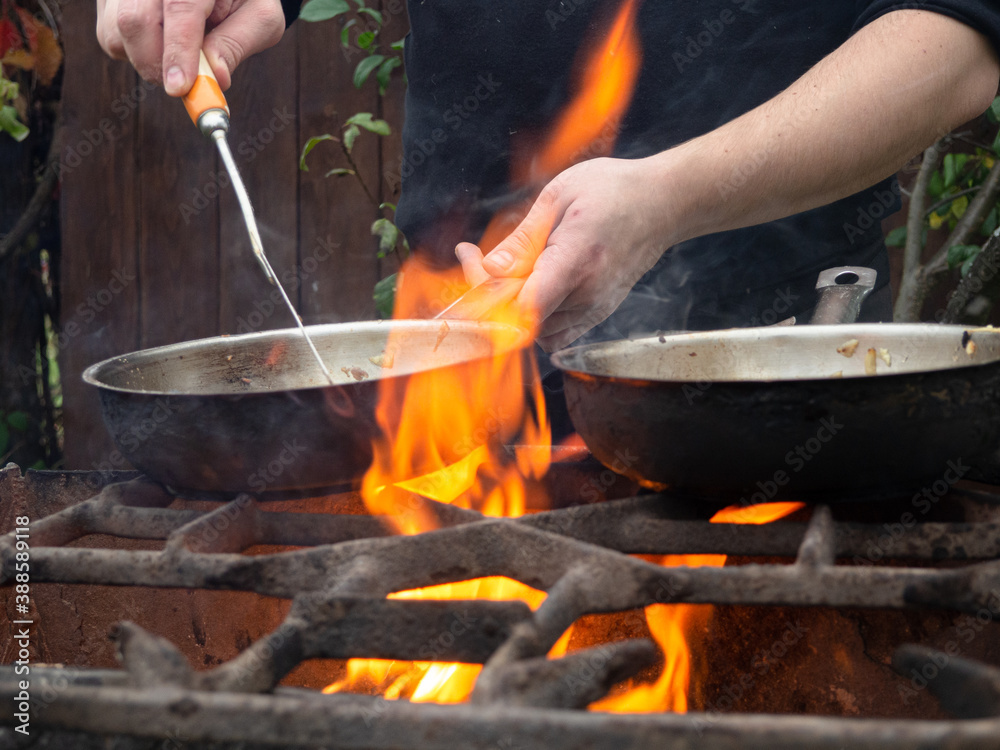 cooking on the grill in a frying pan. frying pan on fire. a man stirs food in a frying pan