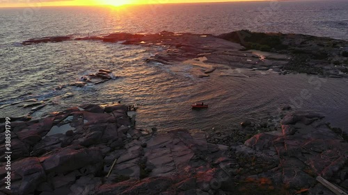 Aerial view of a red boat, anchored at a remote island on the open ocean of the Baltic sea, during a colorful summer sunset, in Scandinavia - tracking, drone shot photo