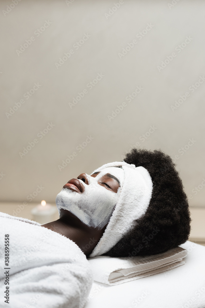 Curly African American woman lying with face mask with blurred candle on background Curly African American woman lying with face mask with blurred candle on background