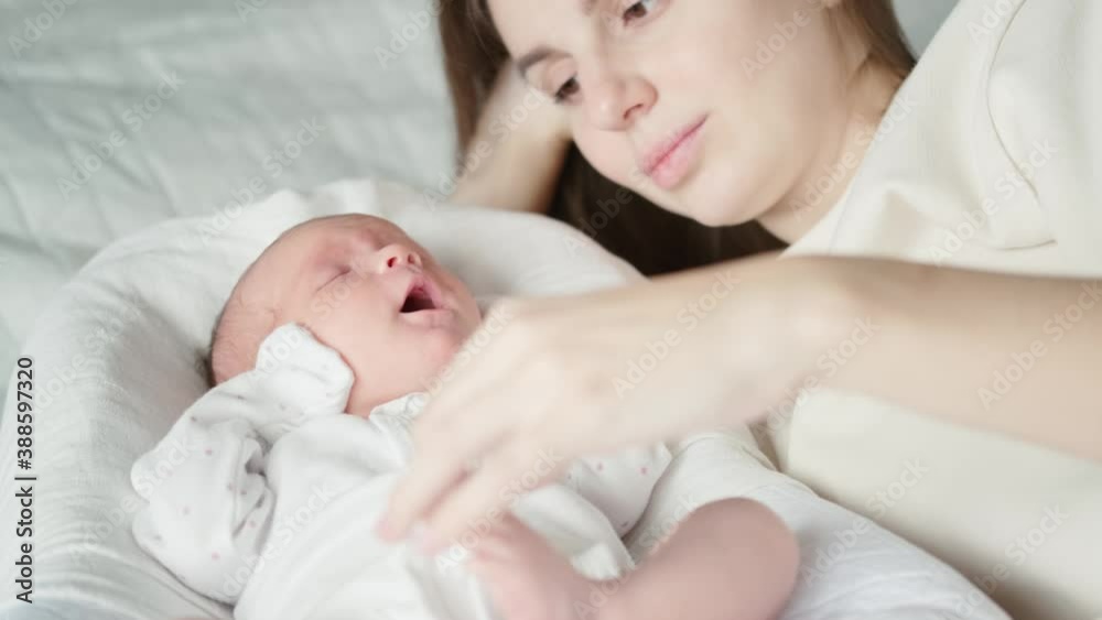 Newborn baby sleeps in its cradle and yawns. Young woman enjoying motherhood and stroking her cute little daughter on the tummy Newborn baby sleeps in its cradle and yawns. Young woman enjoying motherhood and stroking her cute little daughter on the tummy