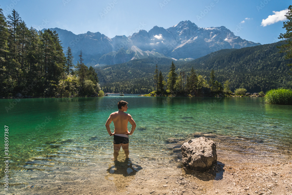 Man in swimwear standing and relaxing in front of a beautiful lake in the Bavarian Alps, Germany, Europe