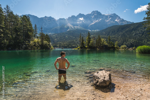 Man in swimwear standing and relaxing in front of a beautiful lake in the Bavarian Alps, Germany, Europe