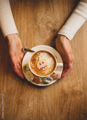 Top view of a cup of latte coffee wrapped in hands with Halloween marshmallows