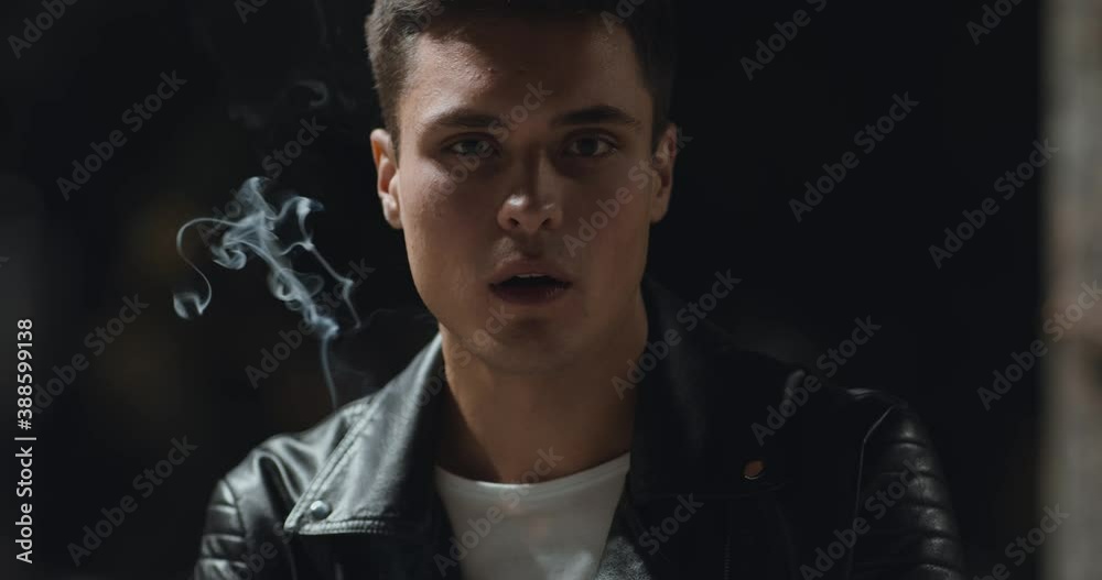 Outdoor portrait of serious man smoking at night park, slow motion