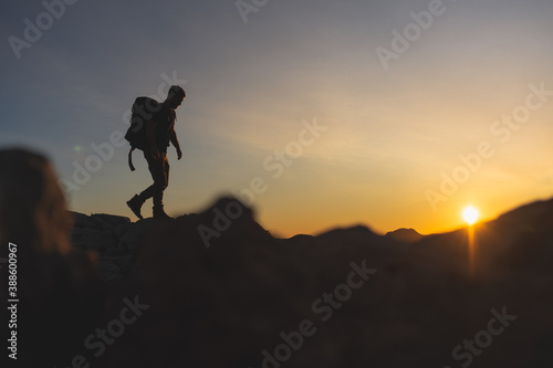 Hiker at the top of a mountain walking on the ridge of the mountain with beautiful golden hour sunset with intense color and blue sky fused with yellow, carrying large backpack